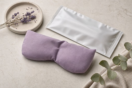 Flat-lay still life of an unbranded single-use fabric eye compress pouch beside its sealed wrapper on a dry surface.