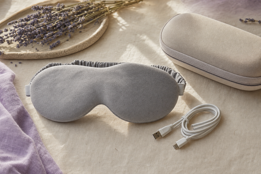 Folded fabric eye mask and coiled charging cable on linen, representing a premium eye-comfort accessory category scene.