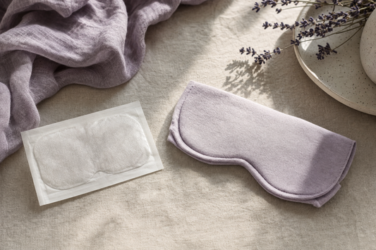 Unbranded disposable eye-mask pouch beside a simply folded cloth mask on linen, representing the steam eye-mask category.