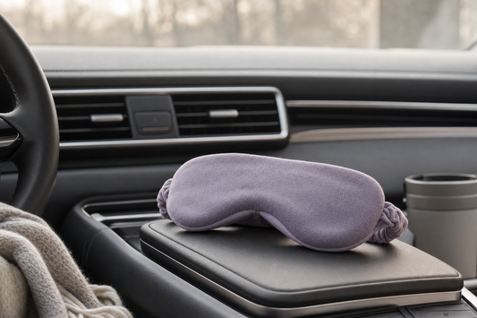 Folded eye mask resting on a car console near a dashboard vent in soft winter daylight, suggesting a pre-drive comfort pause.
